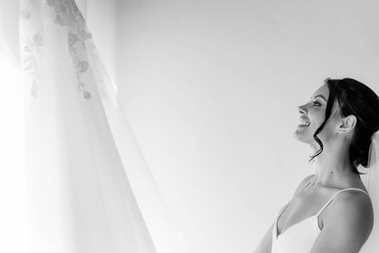 Photographie en noir et blanc de Mathieu Dété, photographe de mariage et famille à Saint-Pierre sur l'île de la Réunion 974, présentant la mariée qui regarde sa robe avant de l'enfiler